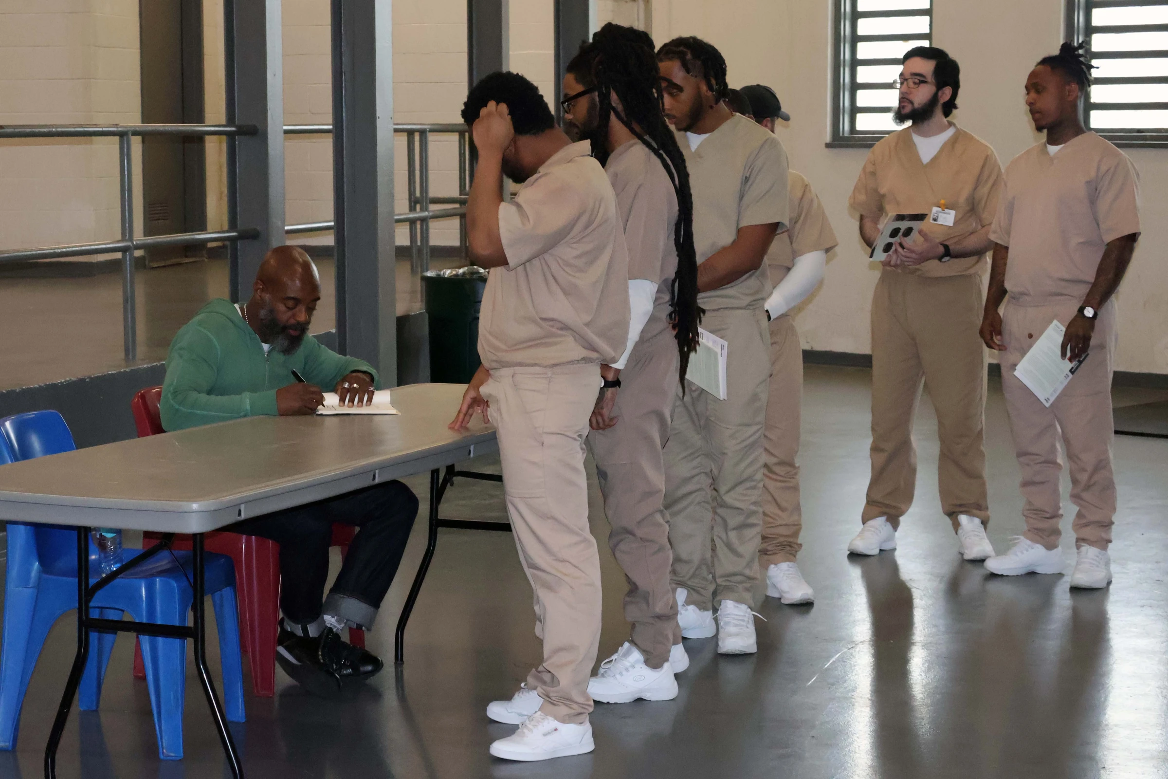 Freedom Reads Founder & CEO Reginald Dwayne Betts signs copies of his book of poetry, *FELON*, after performing at Garden State Correctional Facility in New Jersey. 6 men at Garden State Correctional Facility line up to have copies of FELON signed by Freedom Reads Founder & CEO Reginald Dwayne Betts, who sits at a table.