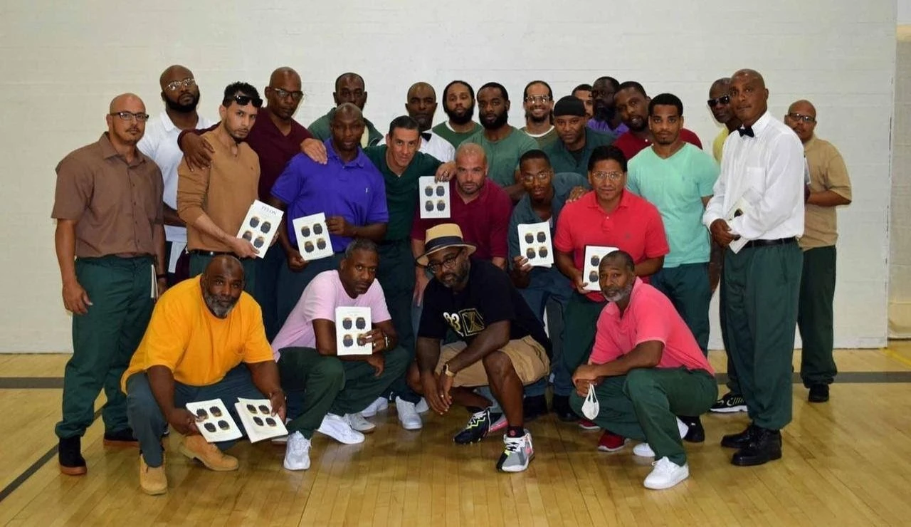 Freedom Reads Founder & CEO Reginald Dwayne Betts, front row in a fedora, with audience members at Otisville Correctional Facility in New York holding copies of Dwayne's poetry collection *FELON*. Freedom Reads Founder & CEO Reginald Dwayne Betts, front row in a fedora, with audience members at Otisville Correctional Facility in New York holding copies of Dwayne's poetry collection FELON.