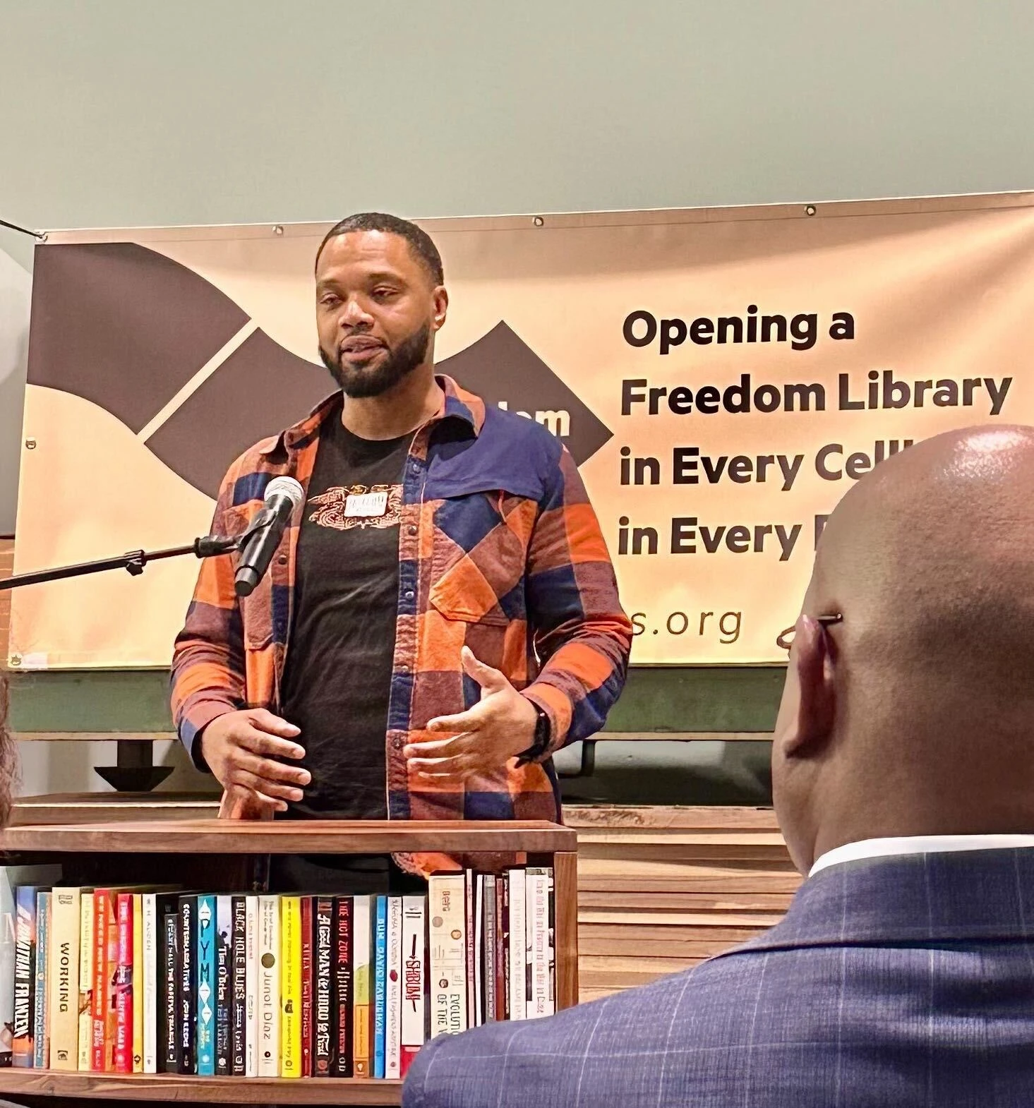 Freedom Reads Library Production Assistant Michael Byrd. Freedom Reads Library Production Assistant Michael Byrd speaks at a microphone in front of a Freedom Library in the Freedom Reads office.