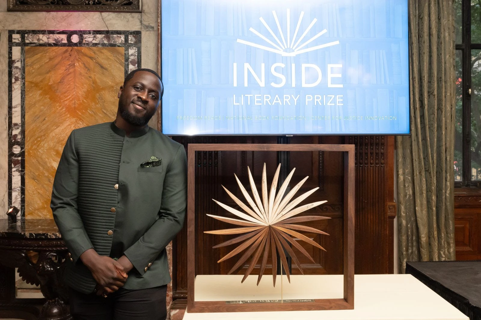 2025 Inside Literary Prize Winner,  Nana Kwame Adjei-Brenyah standing next to Inside Literary Prize award.