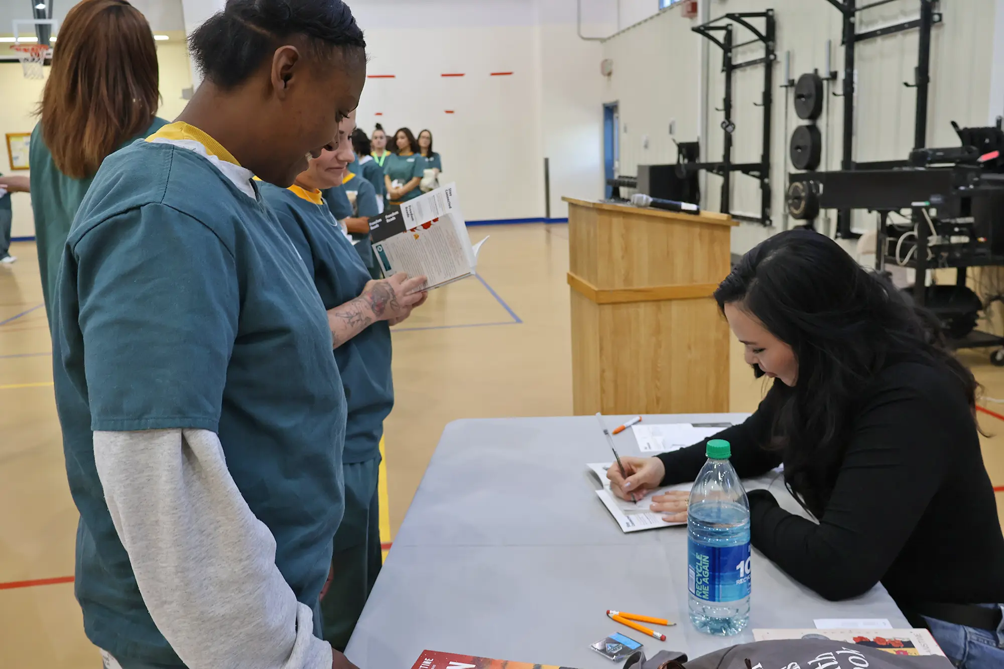 Two women in dark green uniforms smile as Kali Fajardo-Anstine signs books for them at La Vista Correctional Facility in Colorado.